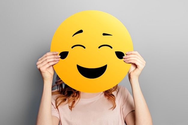 Laughing emoticon with tears of joy Girl holds a yellow smiley with romantic love face