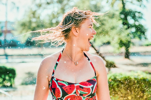 laughing emotional blonde woman with wet hair making water splashes. Holidays, happiness, fun