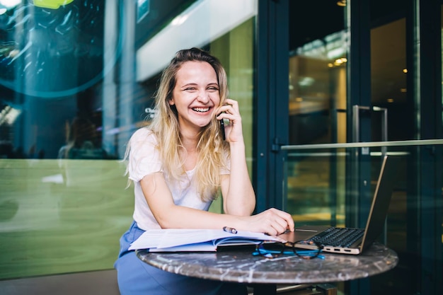 Laughing female talking on phone and using laptop