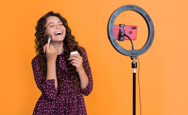 Laughing girl with long curly hair making video for blog hold powder brush