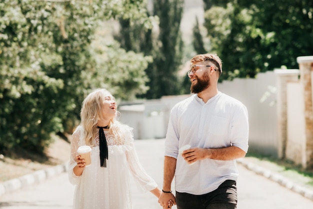 Laughing happy couple holding hands and drinking coffee outdoors on a sunny day