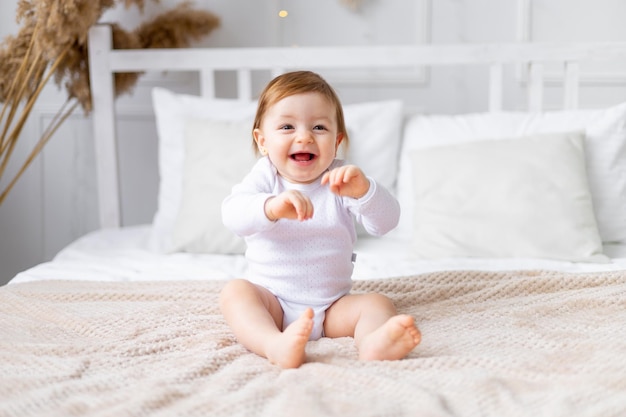 Laughing joyful little baby girl on the bed in a bright room smiling closeup portrait