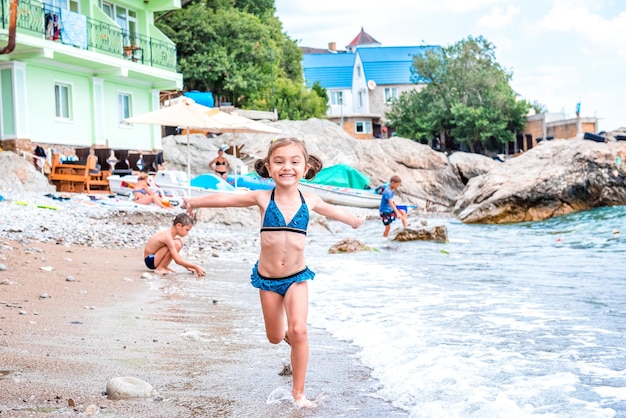 Laughing joyful little girl running away from the waves on the beach near the sea