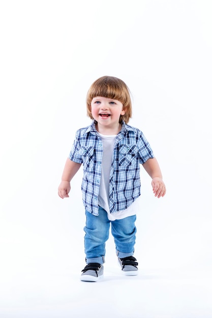 Laughing little boy 2 years old stands Child in jeans and a plaid shirt Curiosity and learning Full height Isolated on a white background Vertical