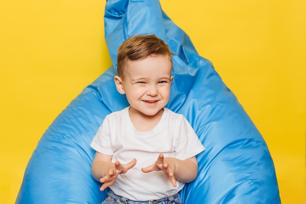 Laughing little boy on a yellow background sitting in a blue chair