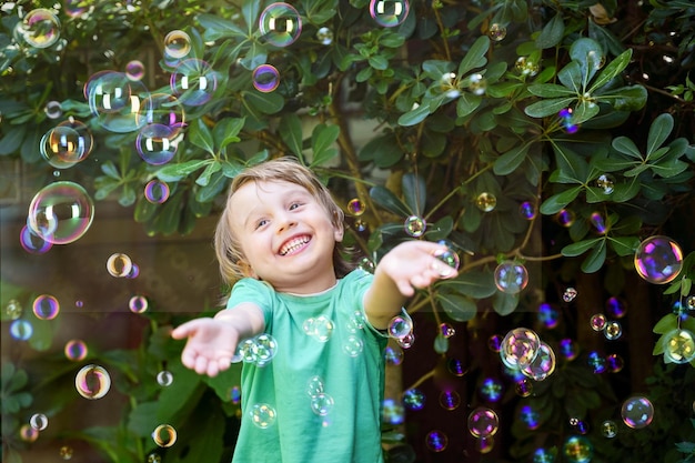 Laughing little toddler boy in the park catches soap bubbles toddler playing outdoors in summer Kids positive emotions