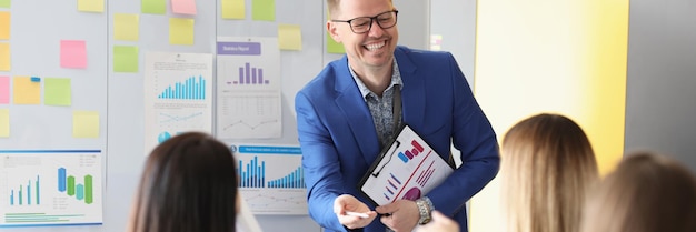 Laughing male speech giver stand in from of colleagues and explain something