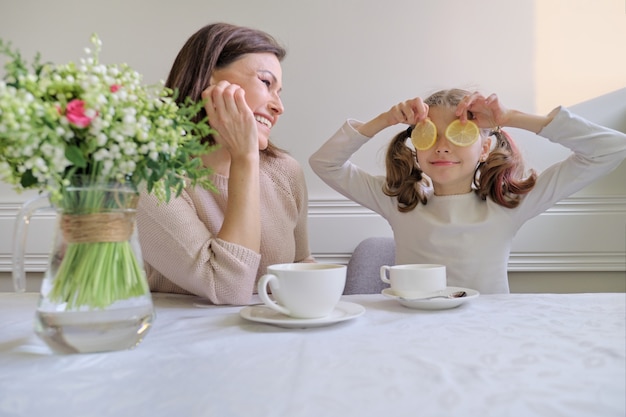 Laughing mother and daughter drinking from cups and eating lemon.