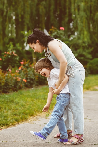 Laughing mum rolls on a back of the small son in park