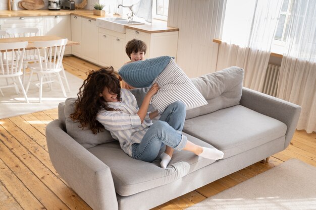 Laughing single mom and little son have fun together happy play childish pillow fight in living room