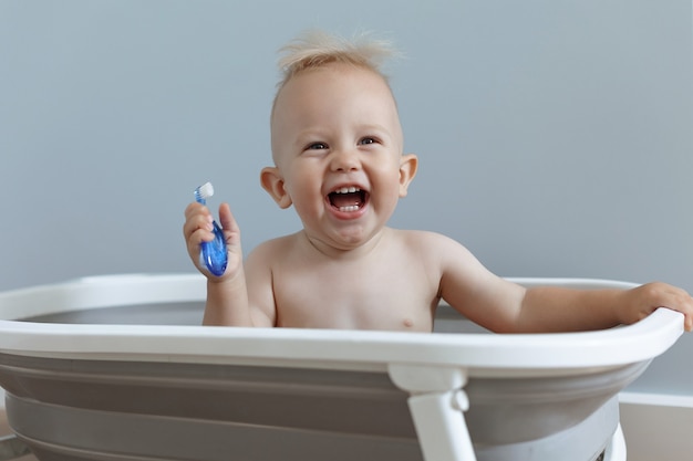 Laughing small child rushes his teeth while sitting in the bathroom