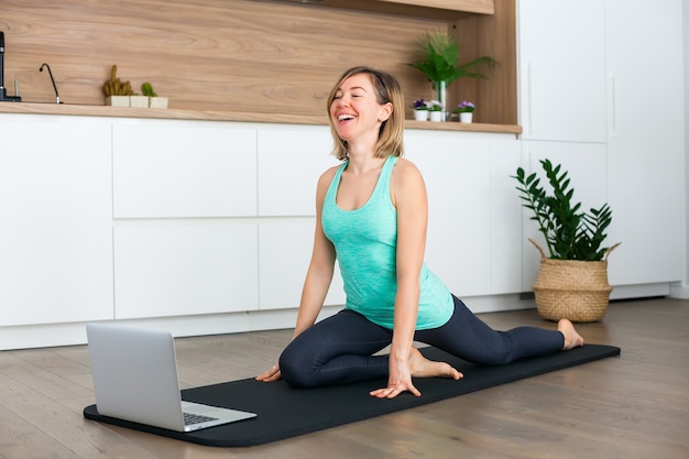 Laughing woman stretching in front of the laptop while doing yoga online at home