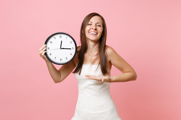 Laughing woman in white dress pointing hand on round alarm clock