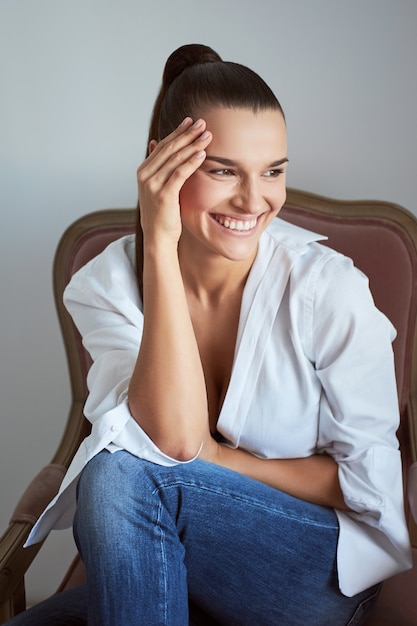 Laughing woman with eyes closed sitting in armchair. Studio shot