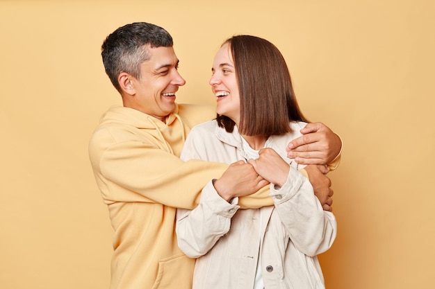 Laughing young couple smiling standing hugging each other looking with charming smiles expressing love and gentle posing isolated over beige background