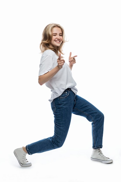 Laughing young girl dances emotionally A teenager in jeans and a white Tshirt Activity movement and positive White background Vertical