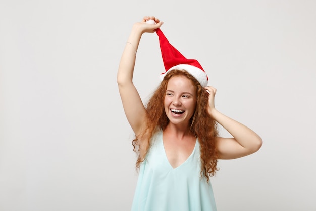 Photo laughing young redhead santa girl in light clothes posing isolated on white wall background studio portrait. happy new year 2020 celebration holiday concept. mock up copy space. holding christmas hat.