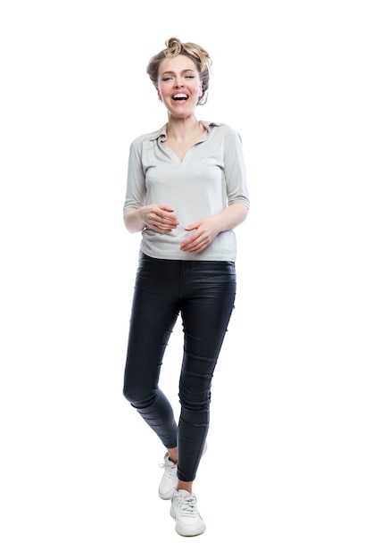 Laughing young woman is standing Beautiful blonde in black leggings gray tshirt and white sneakers Positivity and joy Full height Isolated on white background Vertical