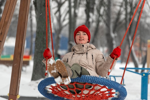 Laughing Young woman rides swing on playground in winter outdoor Girl in warm clothes has fun in outdoors