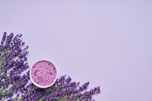 Lavender flowers and bath salt in bowl on lilac backdrop