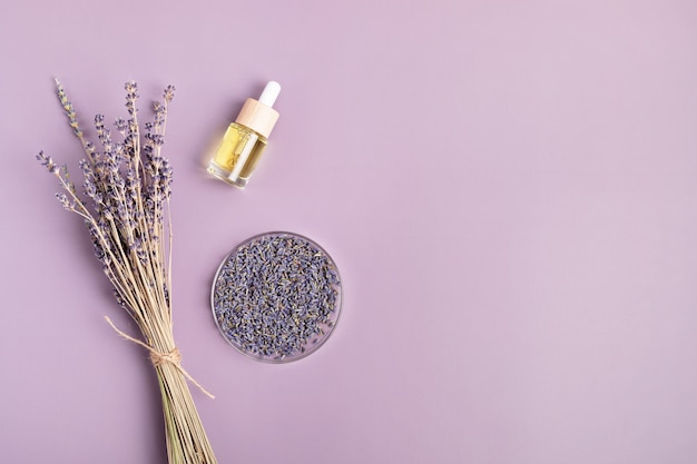 Lavender flowers and herbal essencial oil over purple background. Natural beauty treatment, relaxation, anti stress. Flat lay, top view