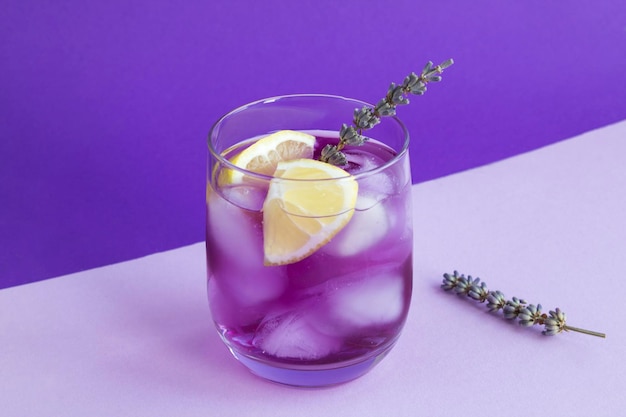 Lavender lemonade with ice and  lemon in the drinking glass on the purple background. Close-up.