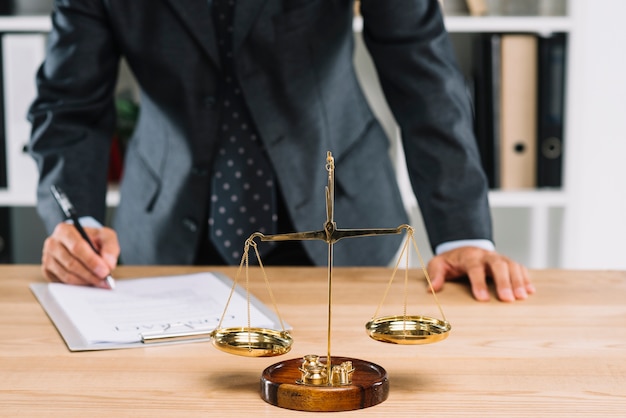 Lawyer signing contract document in front of justice scale over the table