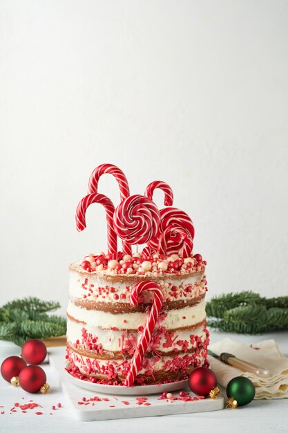 Photo layered christmas gingerbread cake decorated with red lolli pops colored confetti on white cake stand christmas balls fir branches on white concrete table holiday cooking concept selective focus