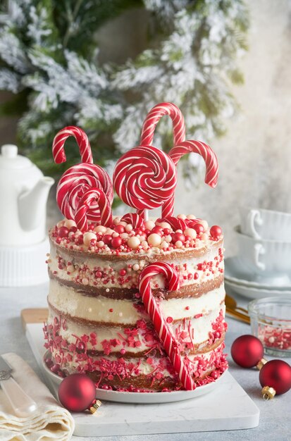 Layered Christmas gingerbread cake decorated with red Lolli pops colored confetti on white cake stand Christmas balls fir branches on white concrete table Holiday cooking concept Selective focus