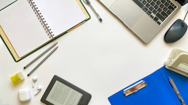 Layout on the topic of education or work on a white background with notepad, pen, laptop, computer mouse, folder for papers, hole punch, headphones, pencils. Flat lay, top view.