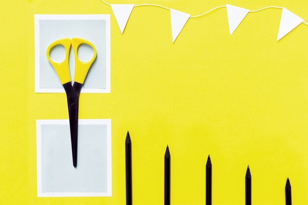 Photo the layout of white paper, black pencils, scissors and white garland on yellow.