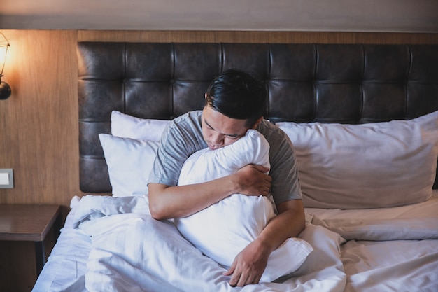 Laziness man sleep while sitting and hugging a pillow on a bed