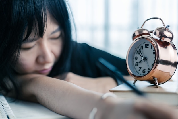 The lazy asian woman lay down in the table with the alarm clock