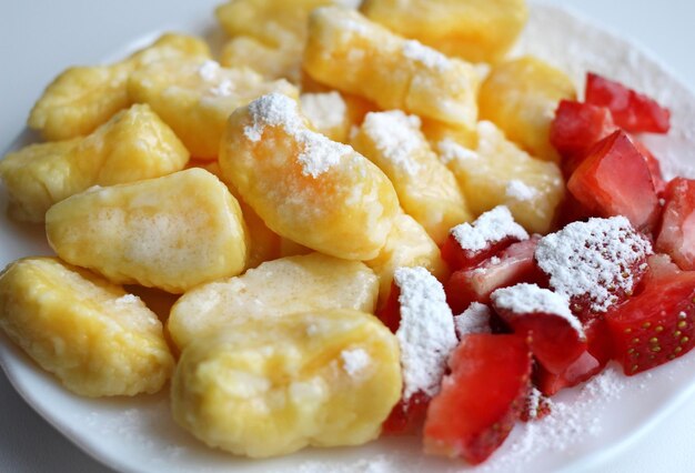 Lazy dumplings with fresh strawberries and powdered sugar on a white saucer