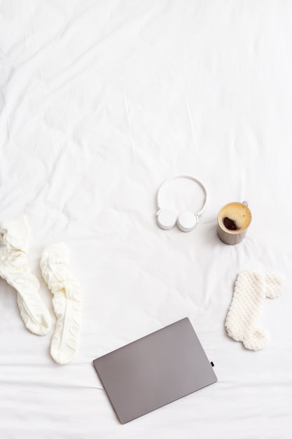 Lazy weekend Morning, Flat lay with laptop, warm socks, cup of coffee, wireless headphones, mask for sleeping on bed