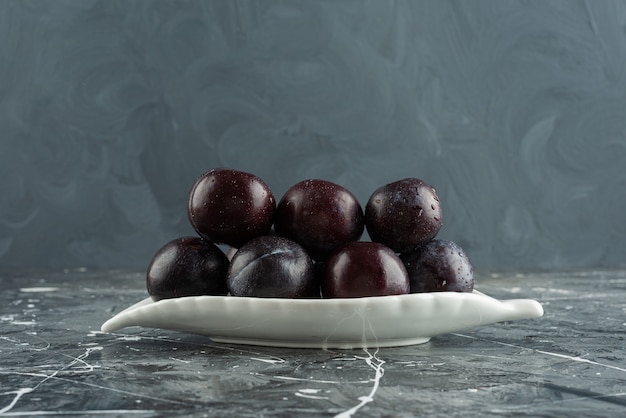 Leaf-shaped plate of fresh plum fruits placed on a marble table .