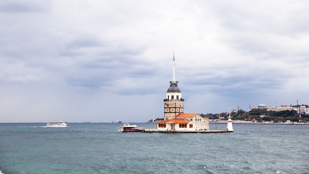 Leander's tower located on the middle of Bosphorus strait, cloudy weather, moving ship and city in the distance Istanbul, Turkey