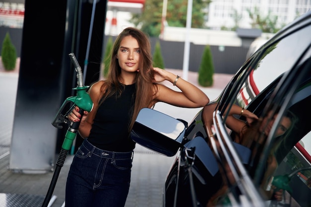 Leaning on the automobile holding pump nozzle A young woman at a gas station with her car