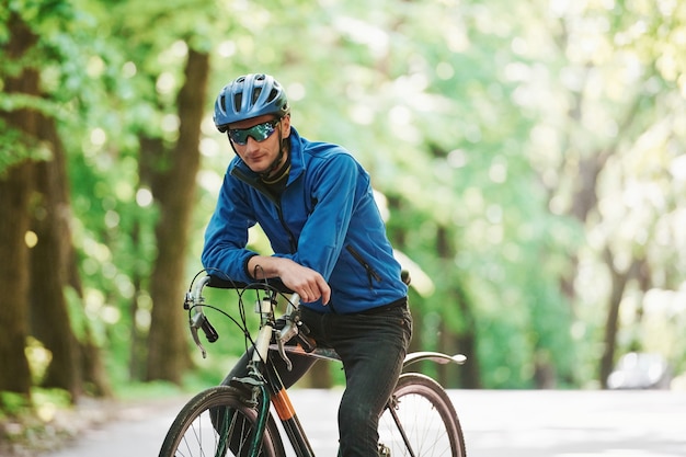 Leaning on the bike. Cyclist is on the asphalt road in the forest at sunny day