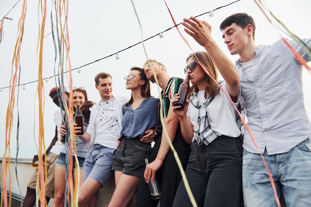 Leaning on the edge of the rooftop with decorates Group of young people in casual clothes have a party together at daytime