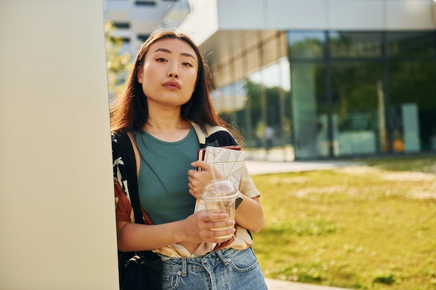 Leaning on the wall Young asian woman is outdoors at daytime