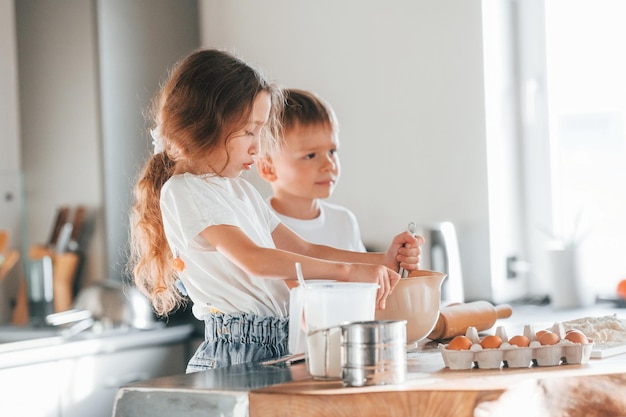 Learning how to cook Little boy and girl preparing Christmas cookies on the kitchen