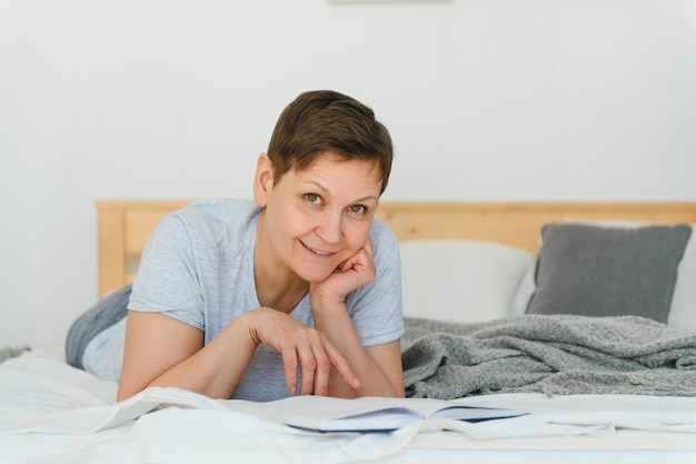 Leasure and home concept smiling middleaged woman reading book and lying on couch at home