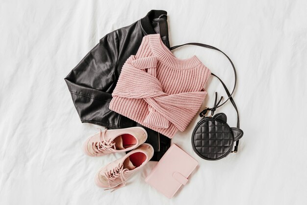 Leather Jacket and Pale pink warm sweater with sneakers, handbag on white sheet. Women's stylish autumn or winter outfit. Trendy clothes collage. Flat lay, top view.