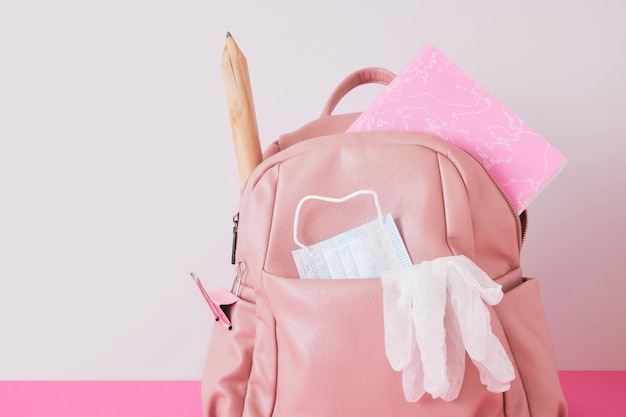 Leather pink backpack on the shoulders on a gray background,, face mask and gloves, lockdown at school