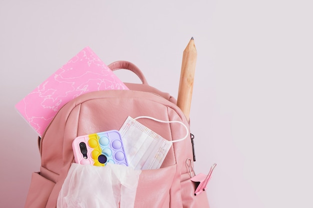 Leather pink backpack with a head, a smartphone with a pop it case, pencil and a notebook, back to school concept