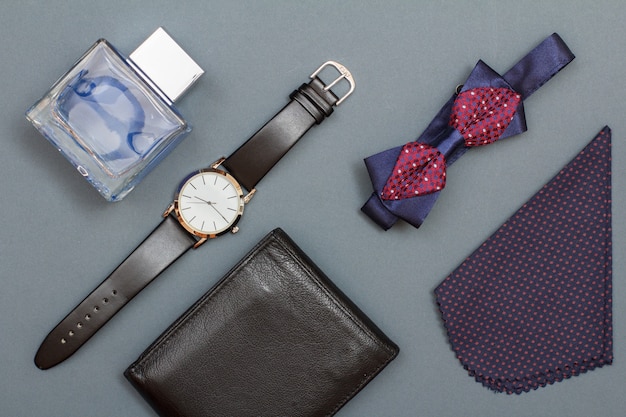 Leather purse, watch with a black leather strap, cologne for men, bow tie and handkerchief on grey background. Accessories for men. Top view