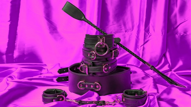 Leather straps handcuffs collar belt and whip on a purple satin sheet