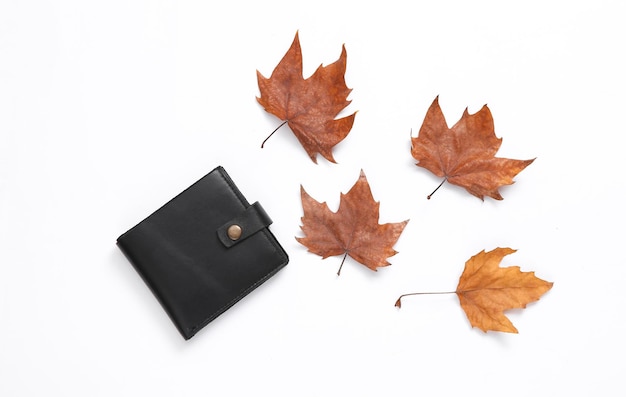 Leather wallet and autumn fallen leaves on white background