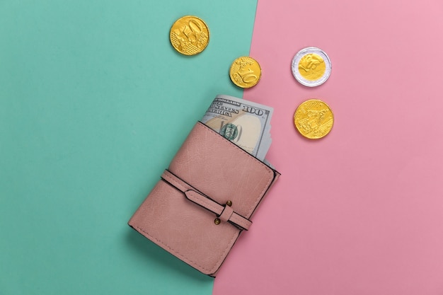 Leather wallet with hundred dollar bills and coins on a blue-pink pastel